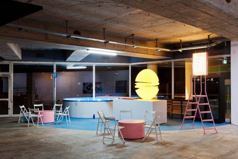 DE: Innenraum des Festivalzentrums mit einem Bartresen, kleinen runden Tischen und Stühlen, sowie einem runden Swimming Pool//EN: EN: Interior of the festival center with a bar counter, small round tables and chairs, and a round swimming pool