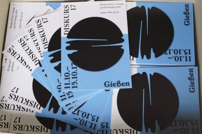 DE: Programmhefte auf denen eine untergehende Sonne vor dem Meer abgebildet ist// EN: Program booklets showing a setting sun in front of the sea